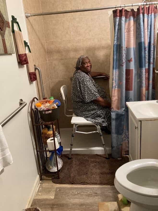 Lady sitting on chair in walk-in shower.
